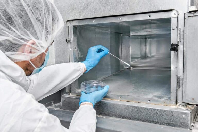 Operatore con DPI esegue un campionamento microbiologico con tampone all’interno di una condotta aeraulica, con piastra Petri in mano