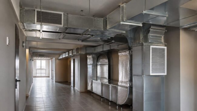 Condotte aerauliche in condominio: canali di ventilazione nelle parti comuni Condotte aerauliche a vista in acciaio zincato nel corridoio delle parti comuni di un condominio