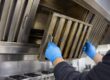 tecnico con guanti in nitrile rimuove un filtro a labirinto coperto di grasso dalla cappa di una cucina professionale durante la pulizia dei canali grassi