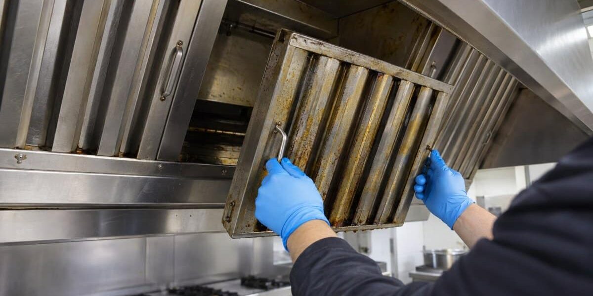 Pulizia canali grassi: rimozione filtro cappa cucina professionale tecnico con guanti in nitrile rimuove un filtro a labirinto coperto di grasso dalla cappa di una cucina professionale durante la pulizia dei canali grassi