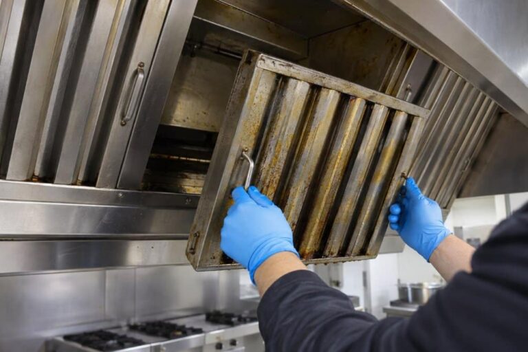 tecnico con guanti in nitrile rimuove un filtro a labirinto coperto di grasso dalla cappa di una cucina professionale durante la pulizia dei canali grassi