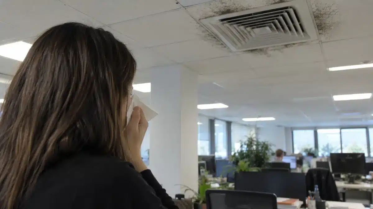 persona in ufficio con fastidio respiratorio vicino a una bocchetta di climatizzazione a soffitto