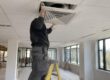 tecnico su scala smonta un diffusore a soffitto coperto di polvere di cartongesso per la pulizia delle condotte dopo una ristrutturazione