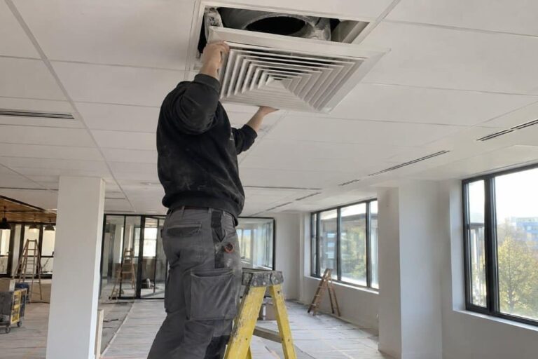 tecnico su scala smonta un diffusore a soffitto coperto di polvere di cartongesso per la pulizia delle condotte dopo una ristrutturazione