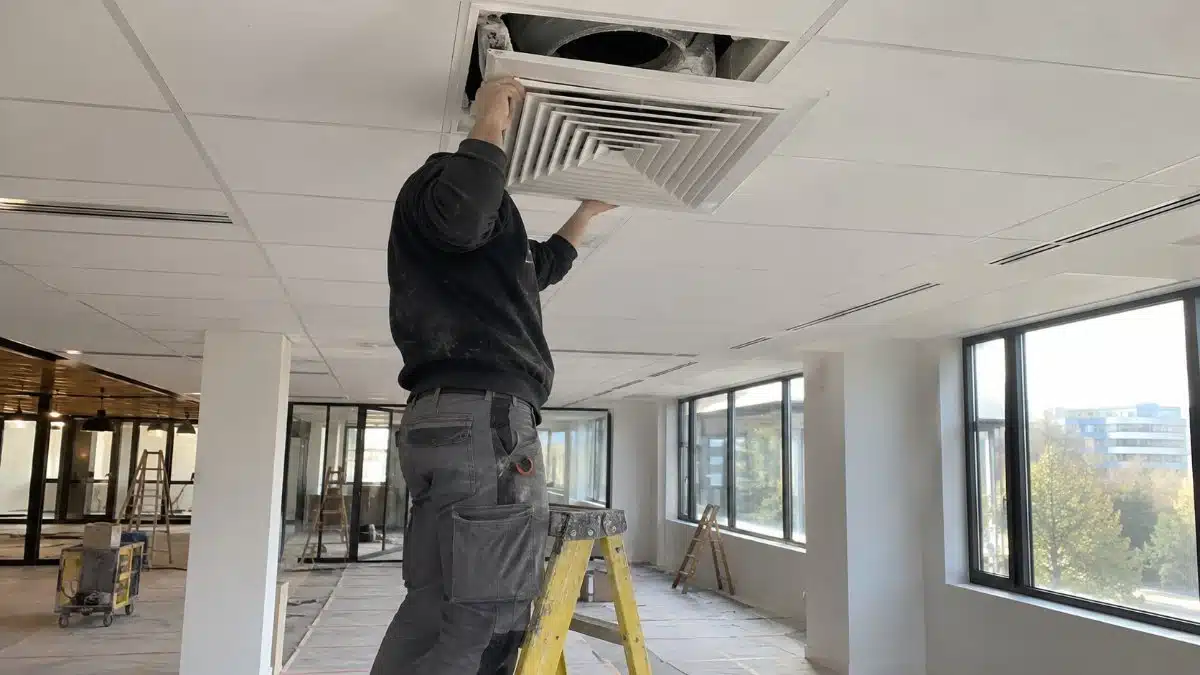 tecnico rimuove un diffusore dell'aria a soffitto coperto di polvere di cantiere in un locale appena ristrutturato