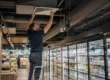 Tecnico ispeziona una bocchetta di aerazione a soffitto in un supermercato durante un intervento di sanificazione delle condotte aerauliche