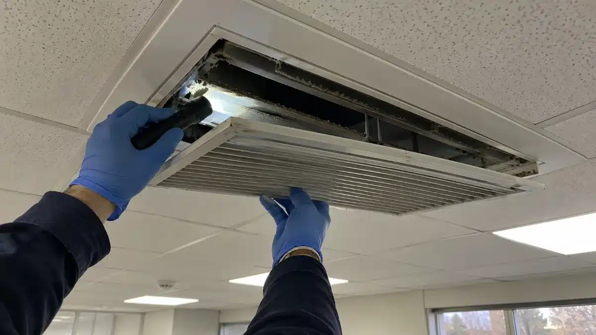 Tecnico verifica con una torcia l'accumulo di polvere vicino a una presa d'aria in una condotta
